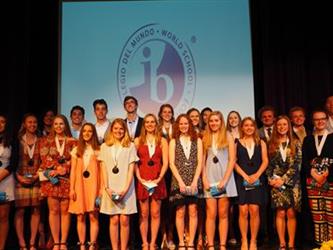 2018 IB graduating class on stage in front of IB logo